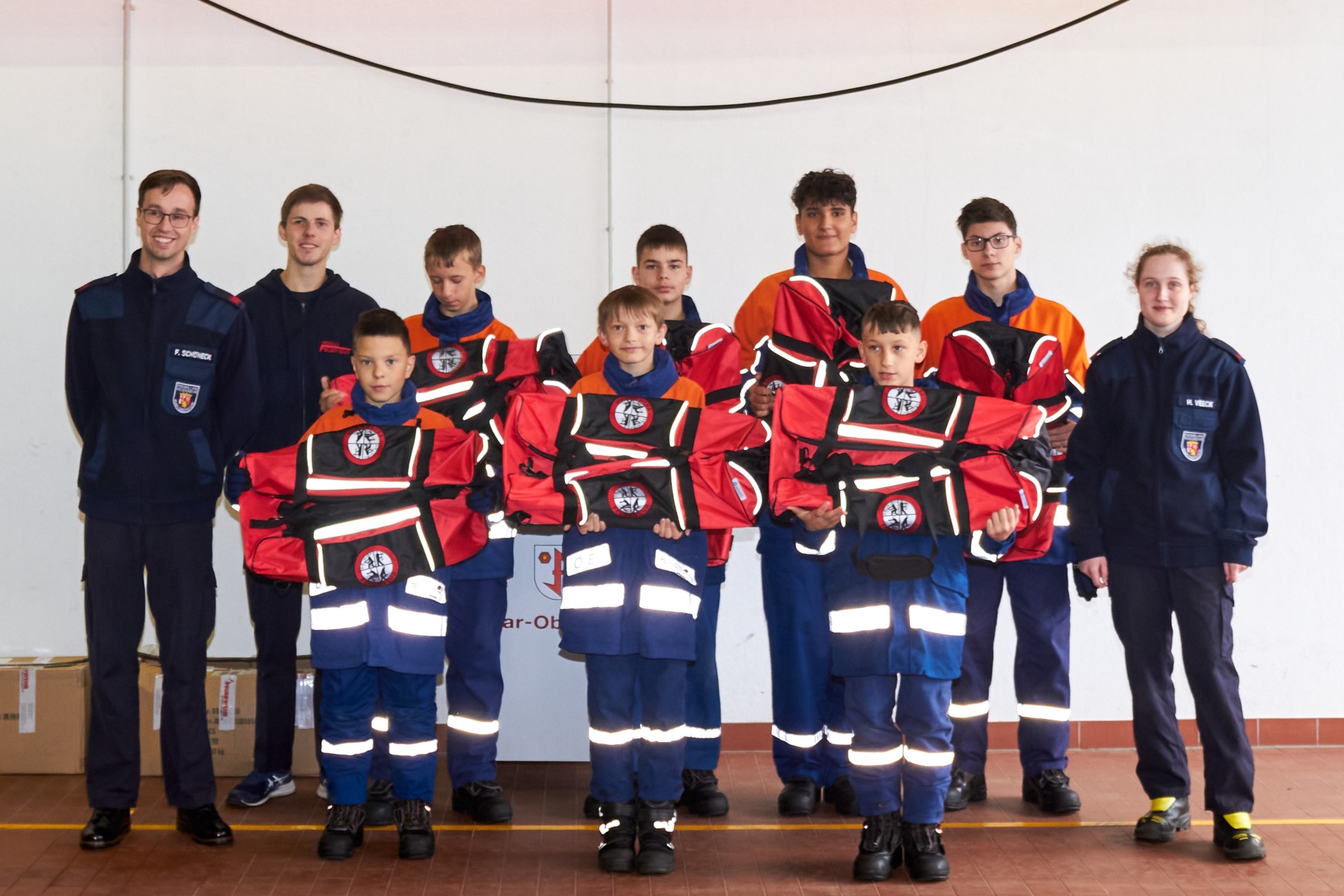 Das Foto zeigt die Mitglieder der Jugendfeuerwehr und ihre Betreuer. Die insgesamt zehn Personen stehen in zwei Reihen vor einer Wand und blicken in die Kamera. Die Jugendlichen halten ihre Einsatztaschen in den Händen.