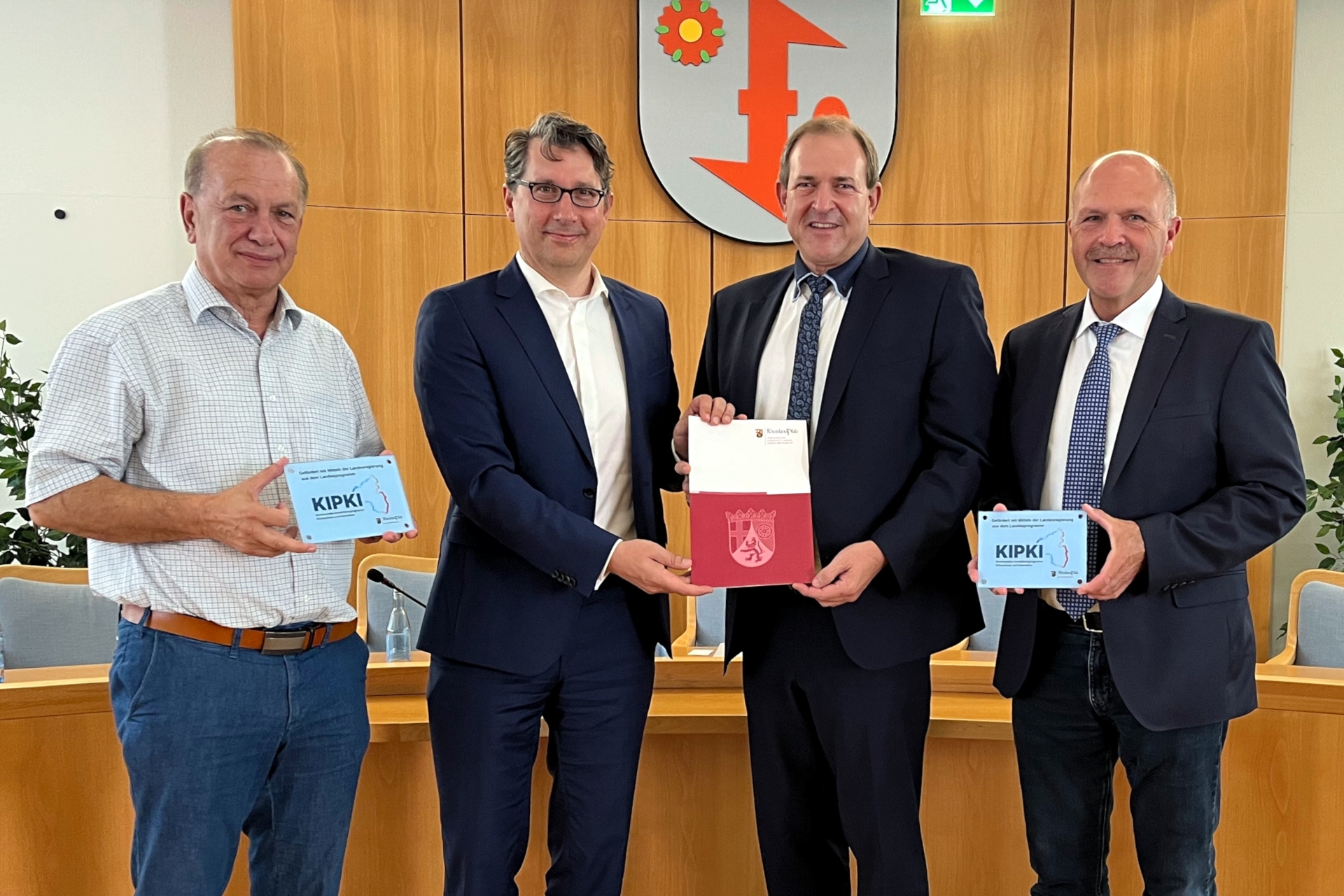 Das Foto zeigt die genannten Personen. Sie stehen im Sitzungssaal nebeneinander und blicken in die Kamera. Staatssekretär und Oberbürgermeister halten gemeinsam den Förderbescheid, Landtagsabgeordneter und Bürgermeister halten jeweils ein KIPKI-Schild.