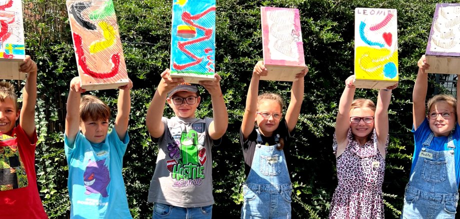 Das Foto zeigt sechs Kinder, die nebeneinander vor einer Hecke stehen und ihre Murmelbahnen über die Köpfe halten.