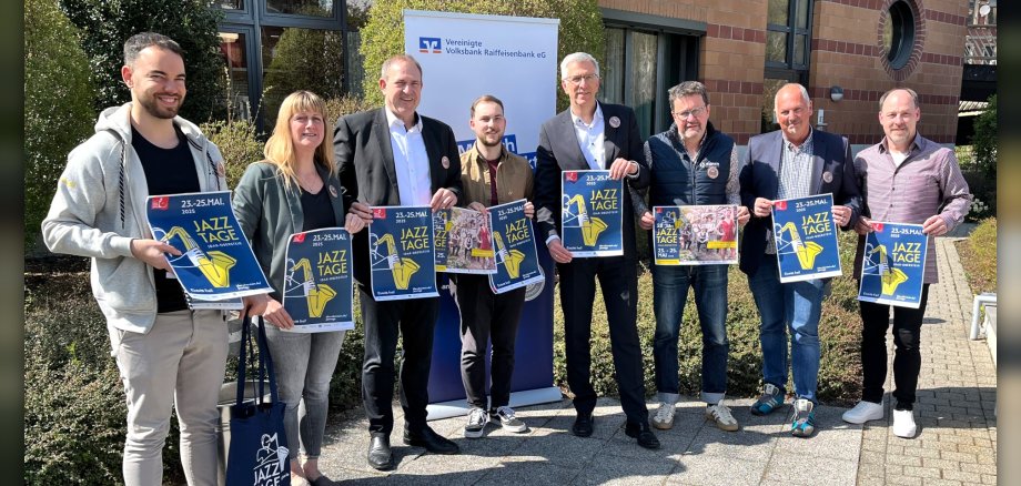 Das Foto zeigt 8 Personen, die im Freien nebeneinander stehen und Plakate der Jazztage in den Händer halten.