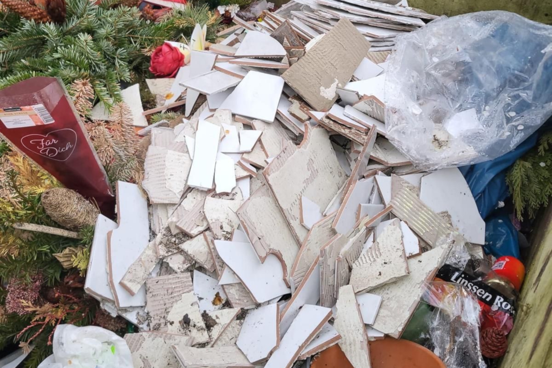 Das Foto zeigt die Müllbox, in der neben den erlaubten Friedhofsabfällen auch eine große Anzahl von weißen Fliesen liegt.