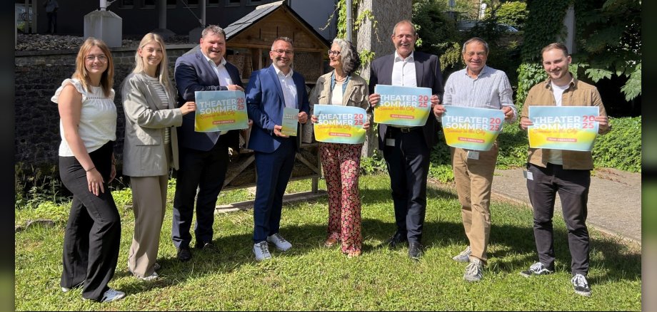 Das Foto zeigt die Organisatoren und Sponsoren. Sie stehen nebeneinander im Garten des OIE-Gebäudes und halten Plakate des Theatersommers in den Händen.
