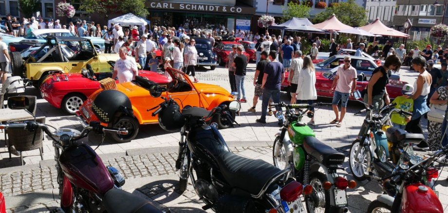 Das Foto zeigt den Idarer Schleiferplatz mit vielen Oldtimern und Besuchern. Auf der Bühne der Konzertmuschel stehen historische Motorräder. 