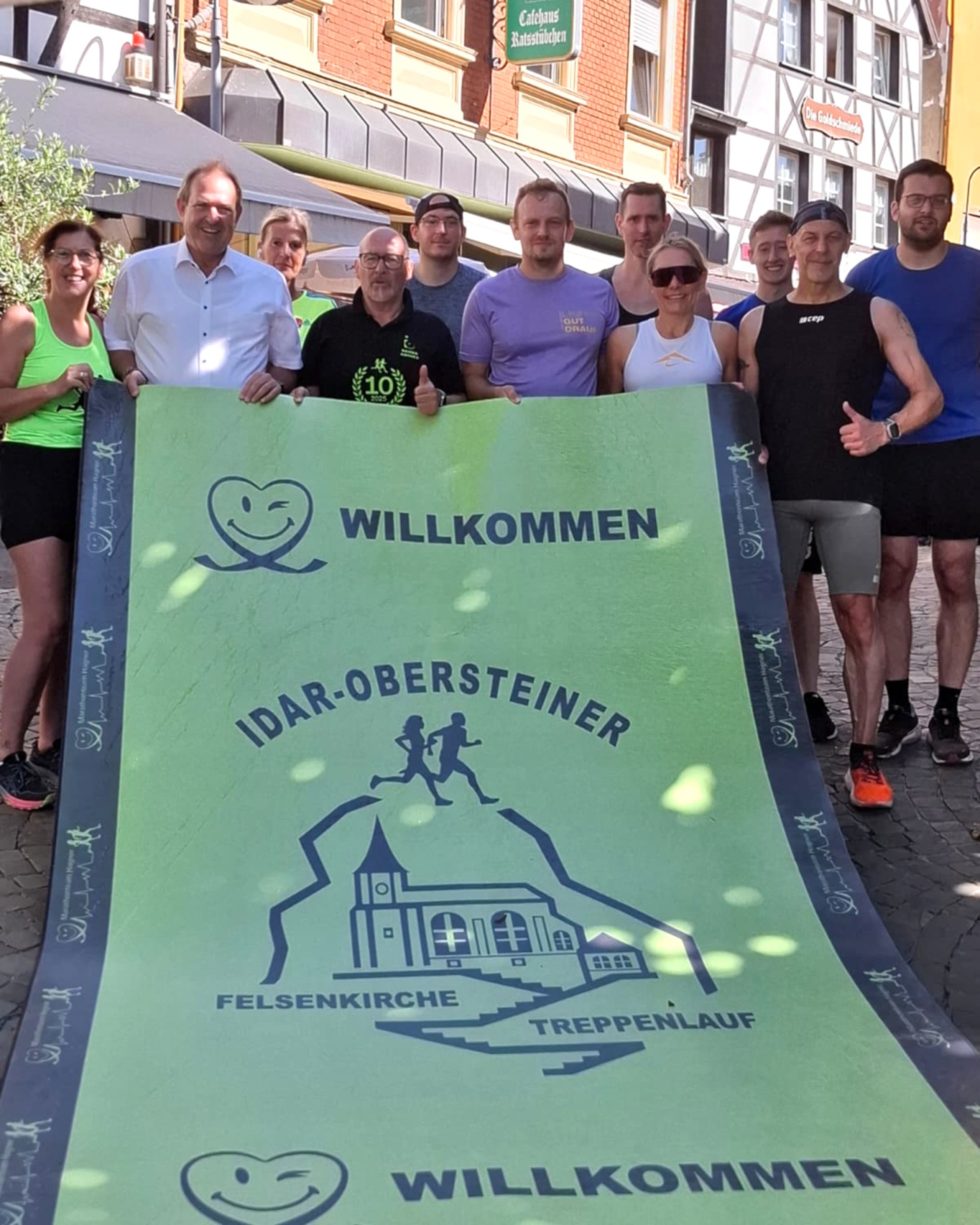 Das Foto zeigt mehrere Personen, die den grünen Einlaufteppich hochheben und in die Kamera halten.