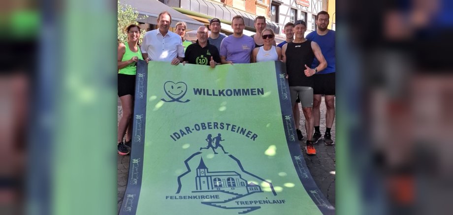 Das Foto zeigt mehrere Personen, die den grünen Einlaufteppich hochheben und in die Kamera halten.