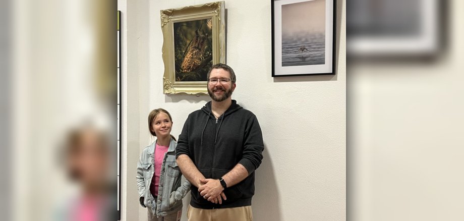 Das Foto zeigt Christopher Norman Schickling mit seiner Tochter vor zwei seiner Fotos. 