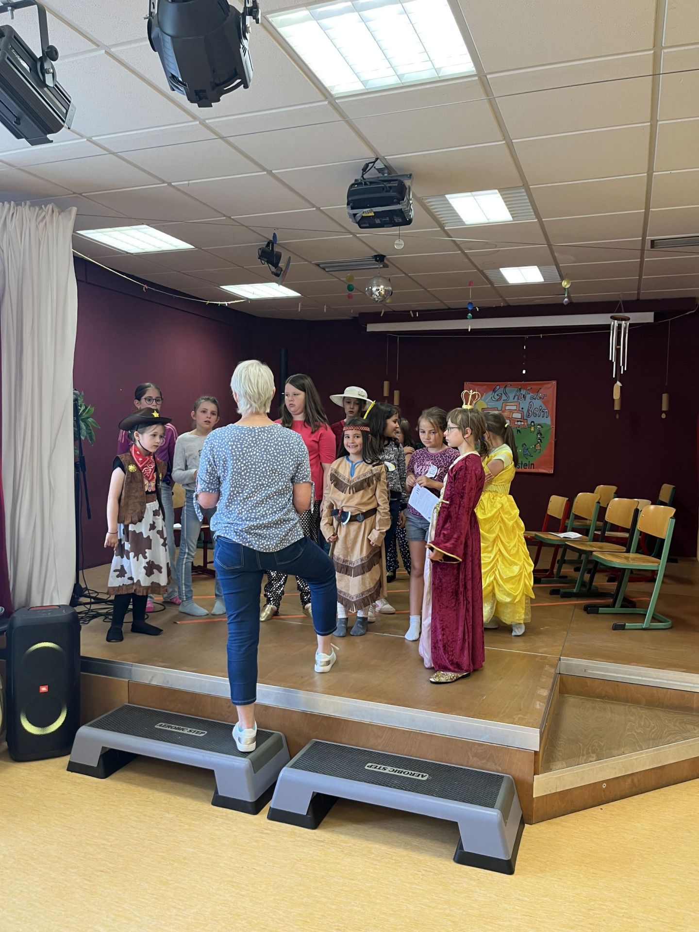 Das Foto zeigt die teilnehmenden Kinder auf der Bühne bei einer Besprechung mit Kerstin Kornetzky. 