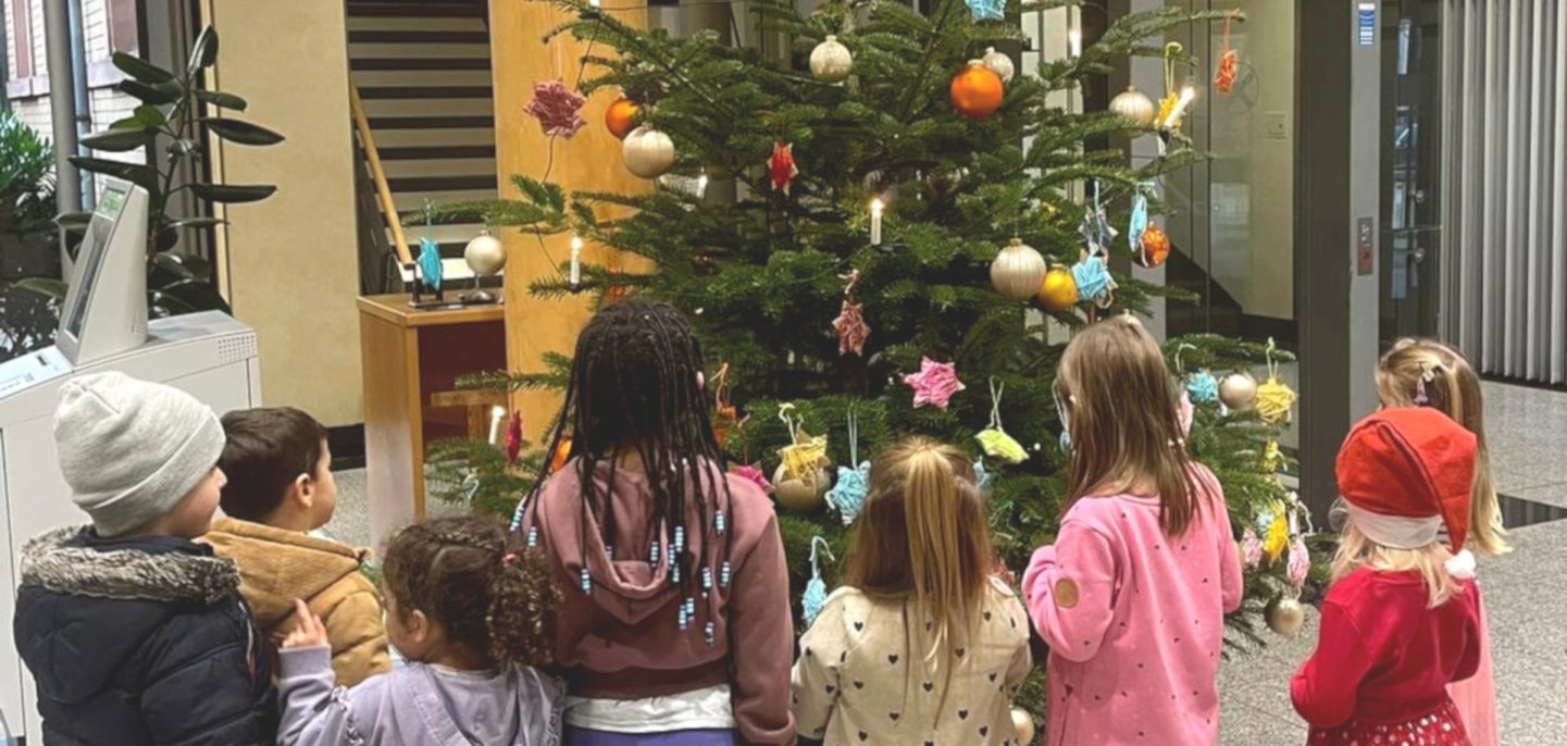 Das Foto zeigt die Kinder, die vor dem geschmückten Weihnachtsaum stehen.
