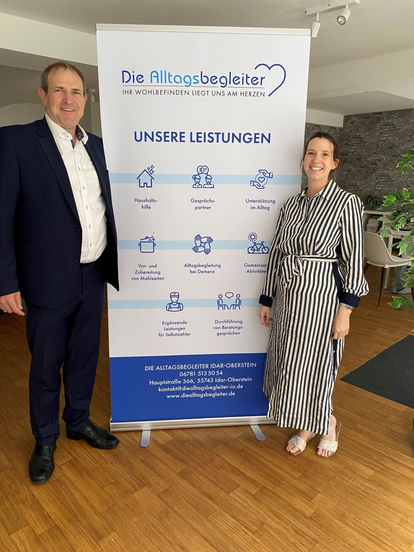 Das Foto zeigt Oberbürgermeister Frank Frühauf und die Geschäftsführerin Selina Dorow neben einem Roll-Up der Alltagsbegleiter. 