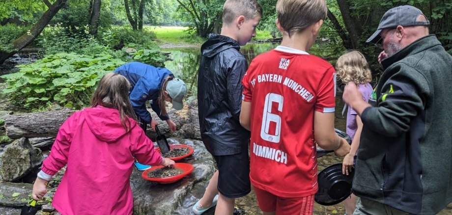 Das Foto zeigt Kinder, die im Bach nach Gold suchen. 