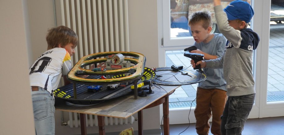 Das Foto zeigt drei Kinder beim Spielen mit einer Carrera Bahn. 