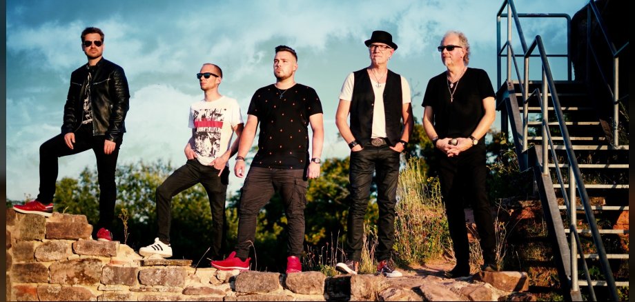 Das Foto zeigt die fünf Bandmitglieder, die auf einer Mauer stehen und in die Ferne blicken.