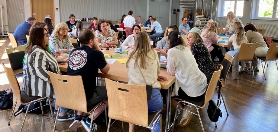 Das Foto zeigt die Teilnehmenden der Konferenz. Sie sitzen an Tischgruppen und diskutieren.
