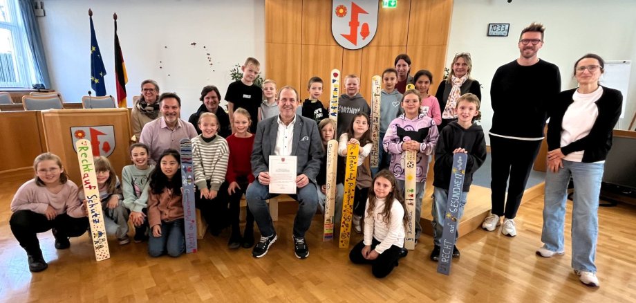Die Grundschule Göttschied übergab Oberbürgermeister Frank Frühauf eine Demokratiebank und einen Zaun der Kinderrechte. Das Foto zeigt die Kinder der Grundschule Göttschied mit dem Oberbürgermeister und Vertretern von Jugendamt und Schule im Sitzungssaal bei der Übergabe.