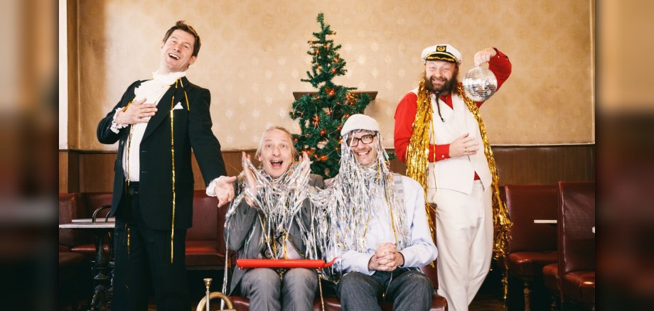 Sebastian Fuchsberger, Leonhard Paul, Michael Horneck und Thomas Gansch (v. l.) bereiten den Besuchern einen humoristischen Liederabend mit wertvollem Kitsch. Das Foto zeigt die genannten Personen die in Kostümen vor einem Weihnachtsbaum stehen bzw. sitzen.