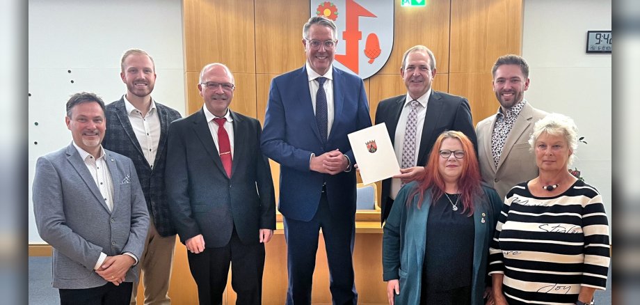 Das Foto zeigt die genannten Personen, sie stehen nebeneinander im Sitzungssaal. OB Frühauf hält den Förderbescheid in der Hand.