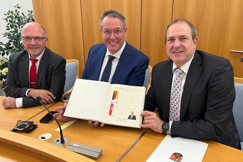Das Foto zeigt Bürgermeister Marx, Oberbürgermeister Frühauf und Ministerpräsident Schweitzer. Der Ministerpräsident präsentiert seinen Eintrag in das Goldene Buch.