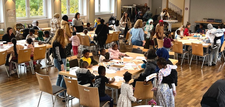 Der Aktionsnachmittag in der Göttenbach-Aula war gut besucht. Das Foto zeigt einen Blick in die Göttenbach-Aula. An Tischen sitzen viele Kinder mit ihren Eltern und den Mitarbeitenden der Ausrichter.