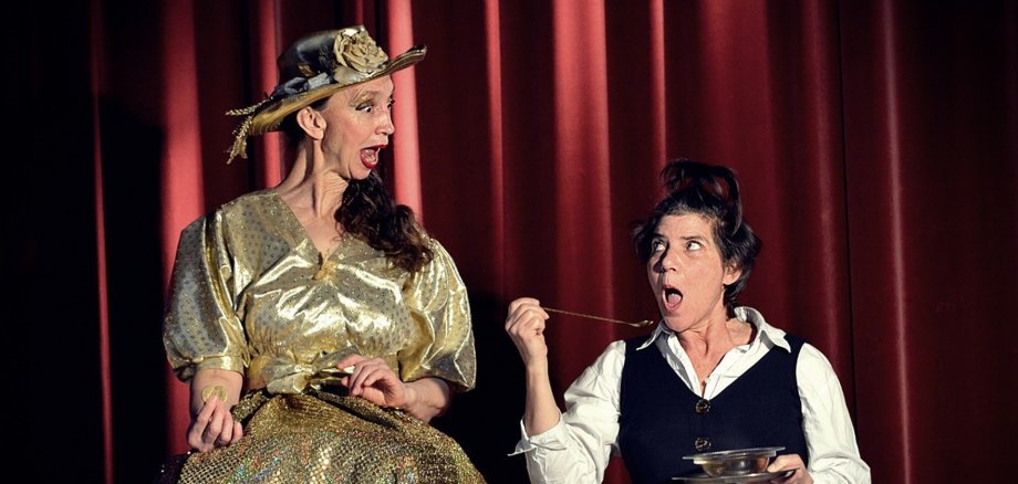 Kathy Becker (l.) und Loraine Iff präsentieren ein witziges und herzerwärmendes Theaterstück rund ums Gold und was im Leben wirklich zählt. Das Foto zeigt eine Spielszene mit den beiden Schauspielerinnen in ihren Kostümen.