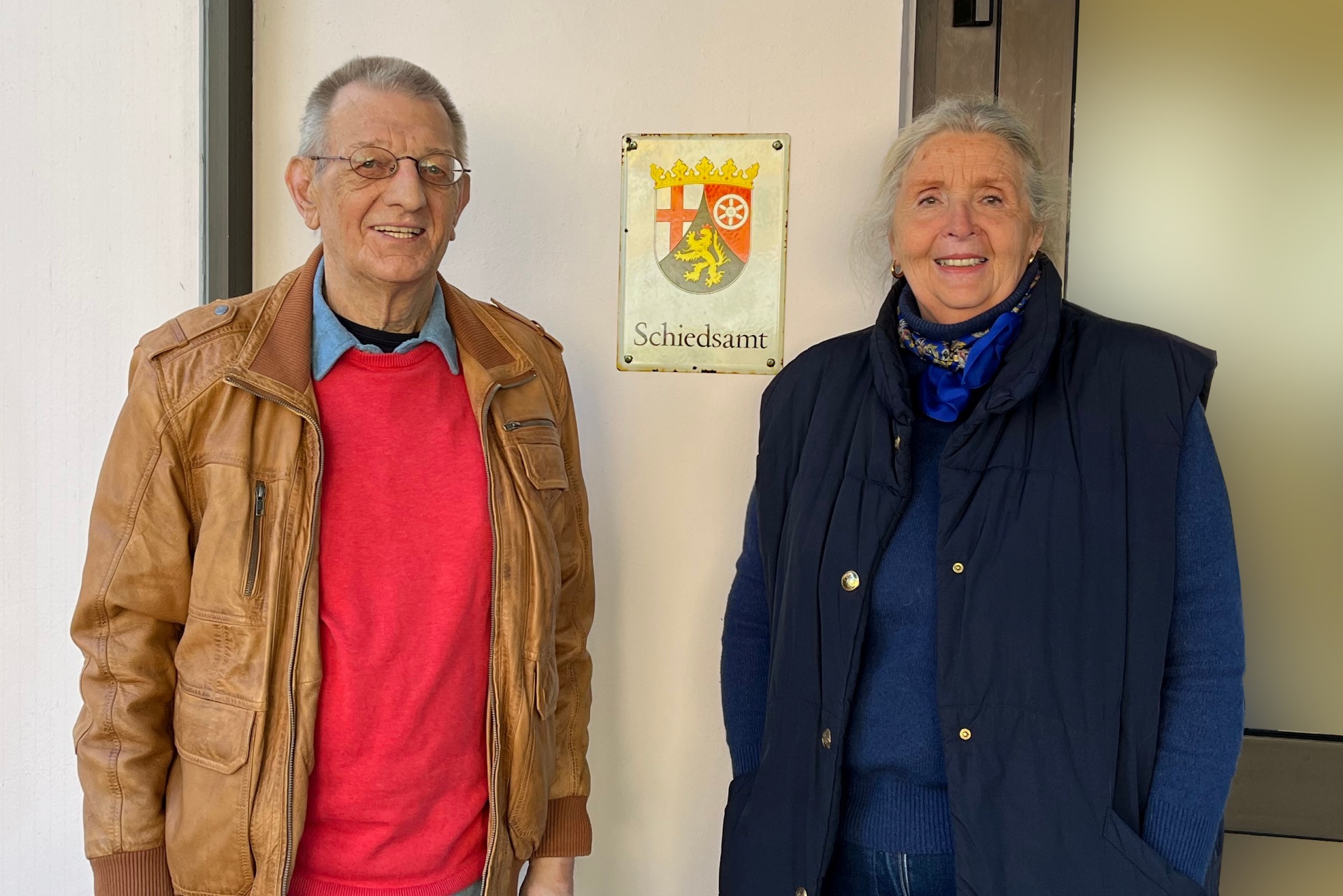 Das Foto zeigt die beiden Schiedspersonen vor dem Schild "Schiedsamt".