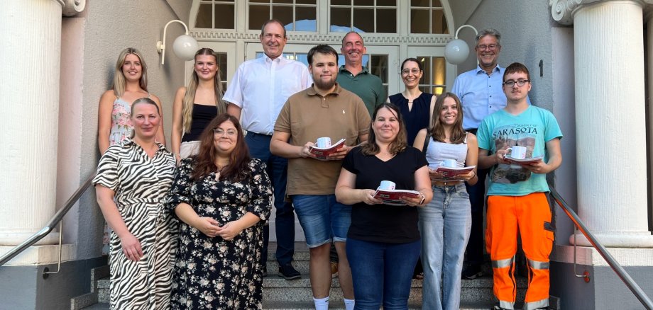 Elena Rudi-Henn, Michelle Meirer, Silas Siebert, Nadine Lang, Zoe Engel und Tyler Roßkopp (vordere Reihe v. l.) wurden bei der Stadt willkommen geheißen – Amani Hfaiedh und Anastasiia Filipova fehlen auf dem Foto. Das Foto zeigt die genannten Personen auf der Treppe vor dem Rathaus.