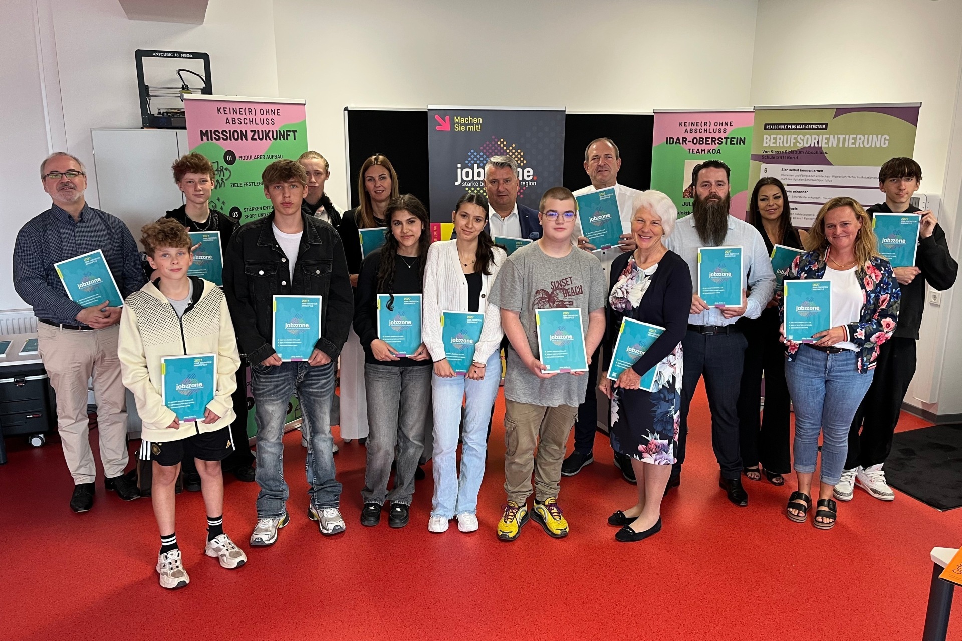 Das Foto zeigt die genannten Personen mit Schülerinnen und Schülern in einem Klassenraum der RS plus.