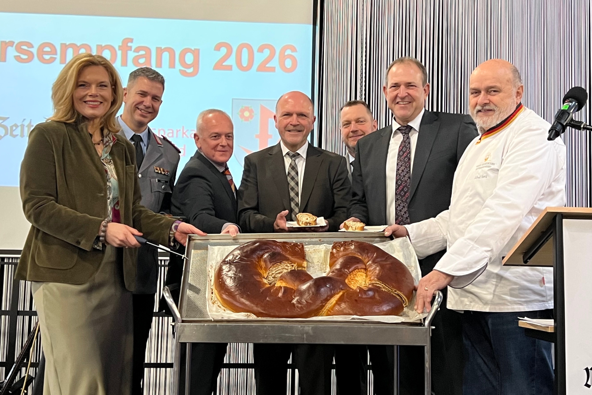 Das Foto zeigt die genannten Personen auf der Bühne in der Messe Idar-Oberstein. Sie präsentieren die große Neujahrsbrezel.