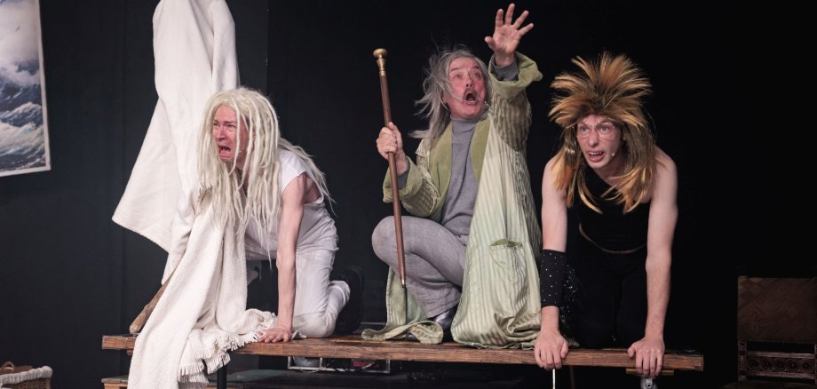 Shakespeares „Der Sturm“ ist ein Stück voll praller Komik und Musik. Das Foto zeigt drei Schauspieler, die kostümiert auf einem Tisch knien.