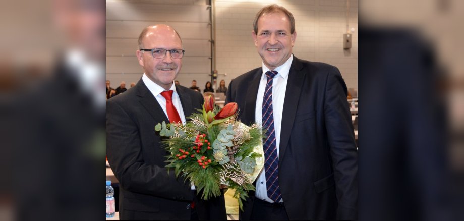 Nach der Wahl durch den Stadtrat – die Sitzung fand Corona-bedingt in der Messe Idar-Oberstein statt – ernannte Oberbürgermeister Frank Frühauf (r.) seinen Stadtvorstandskollegen Friedrich Marx für eine weitere Amtszeit zum Bürgermeister. Das Foto zeigt die beiden Personen in der Messe Idar-Oberstein. OB Frühauf überreicht Bürgermeister Marx einen Blumenstrauß.