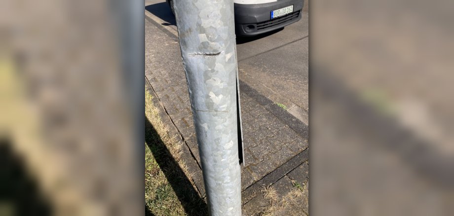 Das Bild zeigt einen Lichtmast, der von einem größeren Fahrzeug beschädigt wurde. 