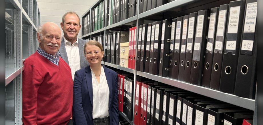 Das Foto zeigt die genannten Personen vor einer Regalwand mit Aktenordnern.